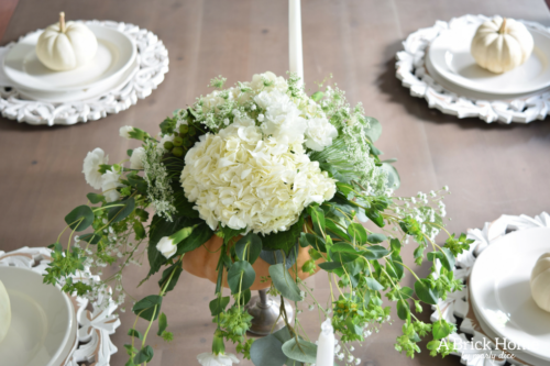 Have YOU seen this gorgeous dining room fall decor with pumpkins and florals? She uses a green and orange color combination to accent her white and silver furniture and decor. Plus, learn how to make this beautiful pumpkin and floral centerpiece. #falldecor #pumpkindecor #falldiningroom
