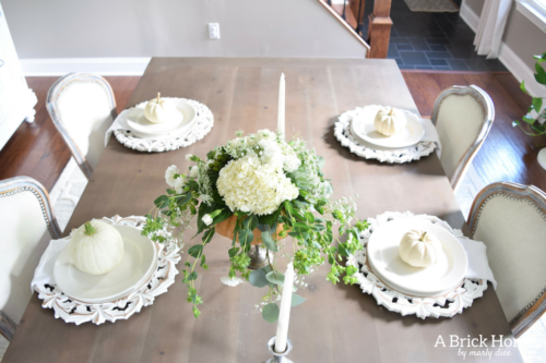Have YOU seen this gorgeous dining room fall decor with pumpkins and florals? She uses a green and orange color combination to accent her white and silver furniture and decor. Plus, learn how to make this beautiful pumpkin and floral centerpiece. #falldecor #pumpkindecor #falldiningroom