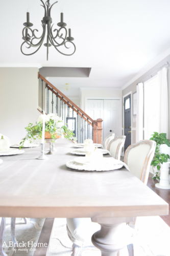 Have YOU seen this gorgeous dining room fall decor with pumpkins and florals? She uses a green and orange color combination to accent her white and silver furniture and decor. Plus, learn how to make this beautiful pumpkin and floral centerpiece. #falldecor #pumpkindecor #falldiningroom