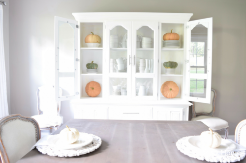 Have YOU seen this gorgeous dining room fall decor with pumpkins and florals? She uses a green and orange color combination to accent her white and silver furniture and decor. Plus, learn how to make this beautiful pumpkin and floral centerpiece. #falldecor #pumpkindecor #falldiningroom