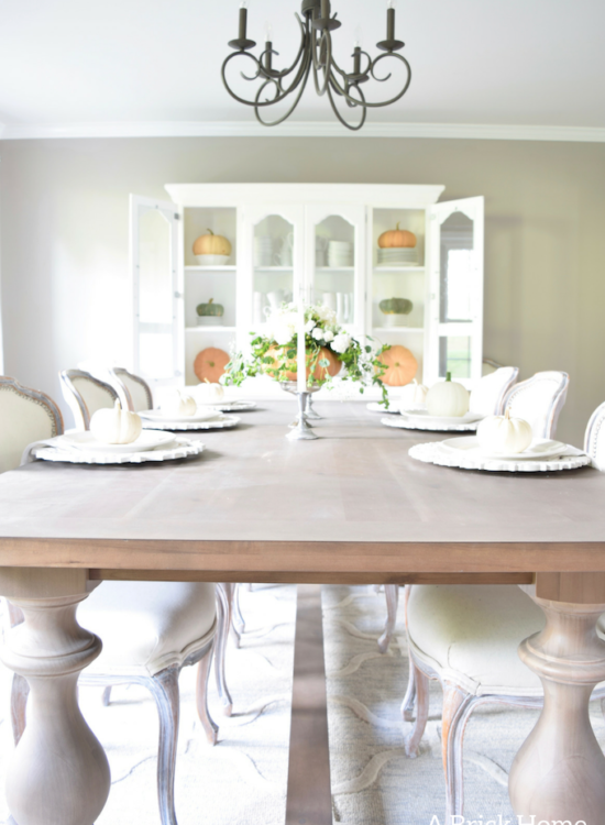 Have YOU seen this gorgeous dining room fall decor with pumpkins and florals? She uses a green and orange color combination to accent her white and silver furniture and decor. Plus, learn how to make this beautiful pumpkin and floral centerpiece. #falldecor #pumpkindecor #falldiningroom