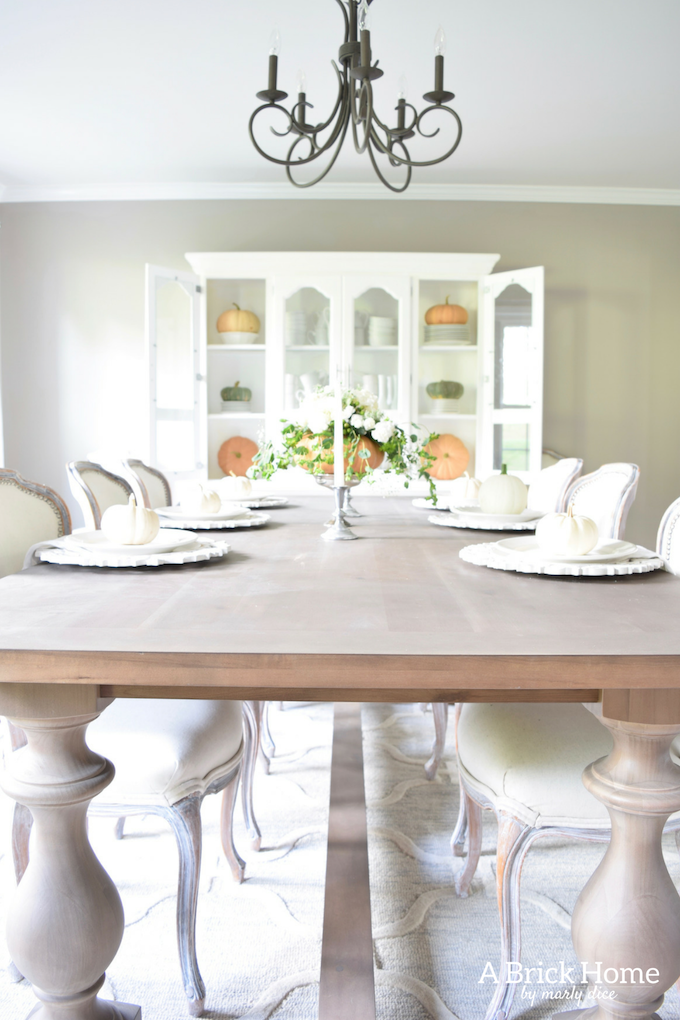 Have YOU seen this gorgeous dining room fall decor with pumpkins and florals? She uses a green and orange color combination to accent her white and silver furniture and decor. Plus, learn how to make this beautiful pumpkin and floral centerpiece. #falldecor #pumpkindecor #falldiningroom