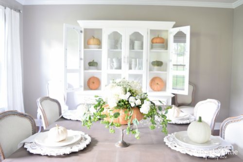 Have YOU seen this gorgeous dining room fall decor with pumpkins and florals? She uses a green and orange color combination to accent her white and silver furniture and decor. Plus, learn how to make this beautiful pumpkin and floral centerpiece. #falldecor #pumpkindecor #falldiningroom