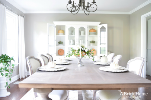 Have YOU seen this gorgeous dining room fall decor with pumpkins and florals? She uses a green and orange color combination to accent her white and silver furniture and decor. Plus, learn how to make this beautiful pumpkin and floral centerpiece. #falldecor #pumpkindecor #falldiningroom